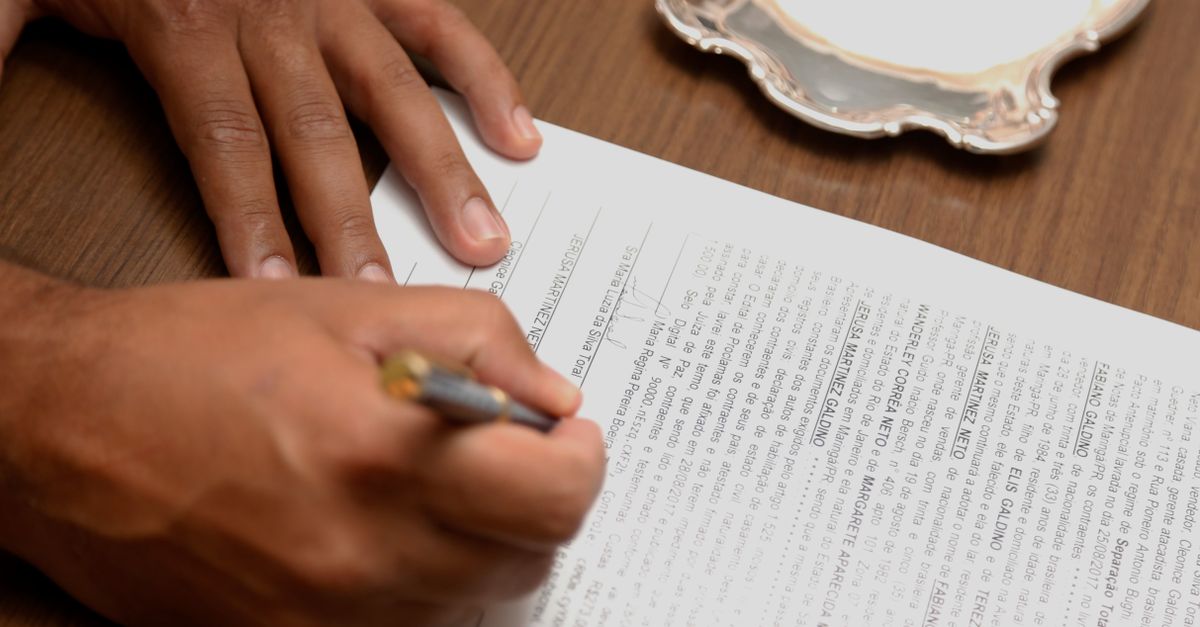Hand signing a contract on a wooden desk, emphasizing business formalities.